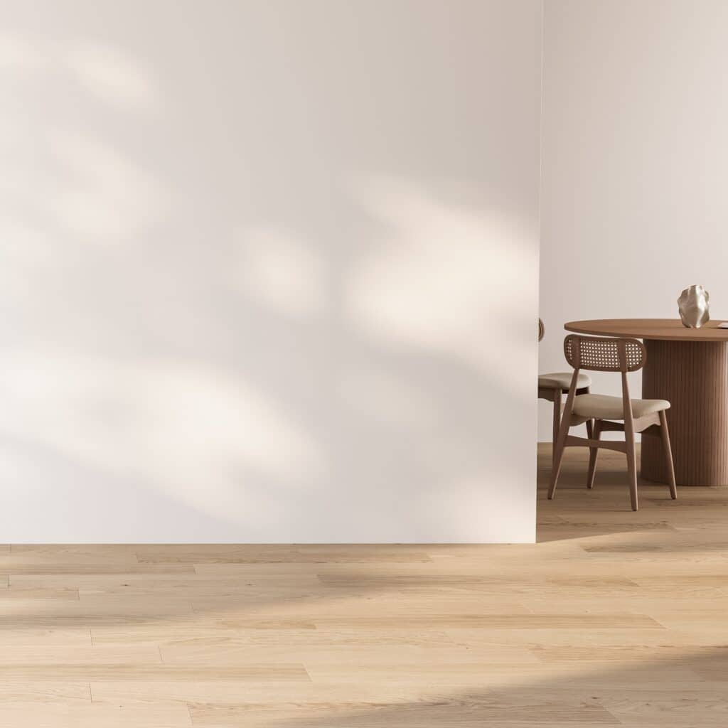 Mur blanc minimaliste, ombres ensoleillées, parquet clair et coin repas avec table ronde et chaises en rotin.