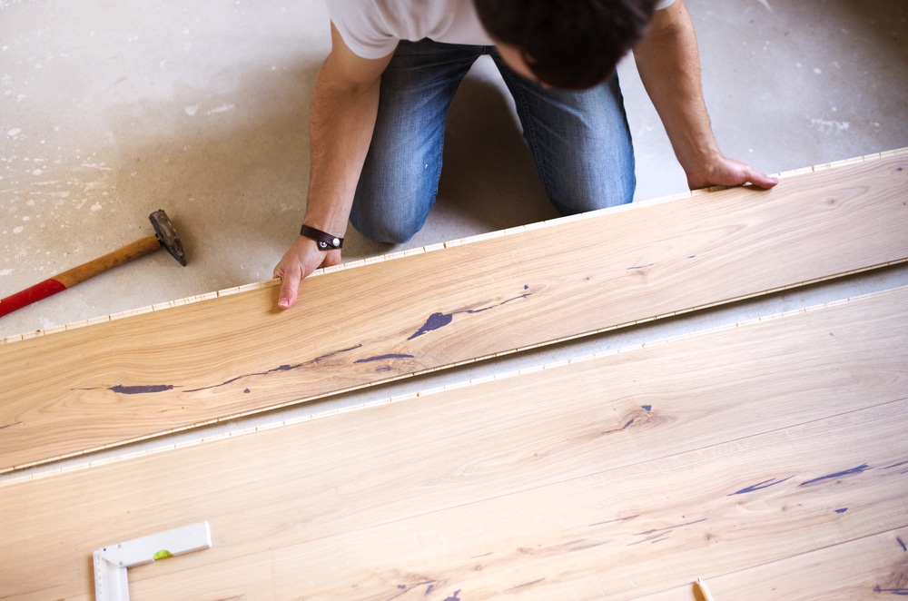 Poseur installant des lames de parquet en bois clair au sol avec un marteau et une équerre pour une rénovation de maison.