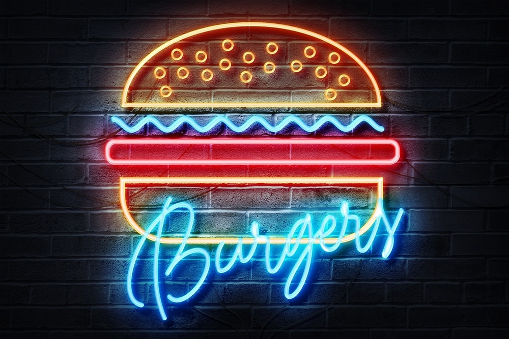 Enseigne Néon Burger : Déco Restaurant Fast-Food Vintage Enseigne néon de hamburger coloré avec texte Burgers en bleu sur un mur de briques sombres style rétro.