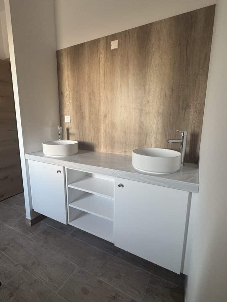 Meuble Double Vasque Moderne Design Bois et Blanc Double vasque blanche posée sur meuble design blanc et bois avec rangements ouverts pour salle de bain.