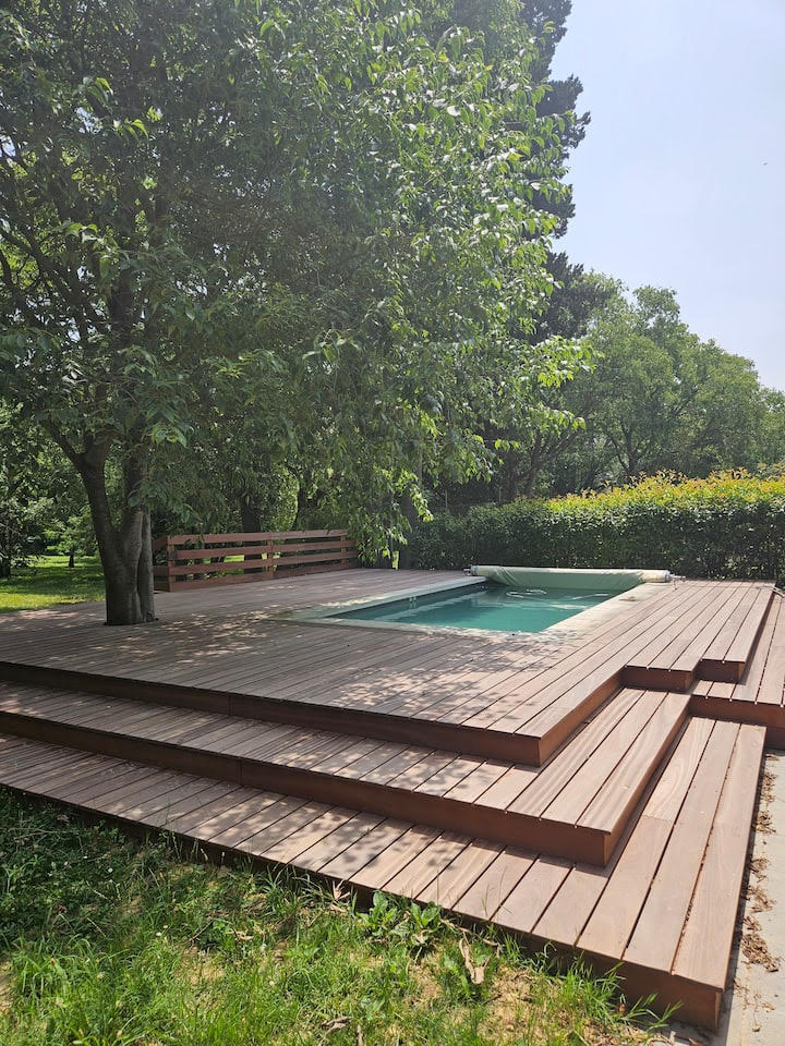 Terrasse en bois avec piscine intégrée et jardin ombragé Piscine intégrée dans une terrasse en bois sous un arbre ombragé dans un jardin verdoyant et ensoleillé.