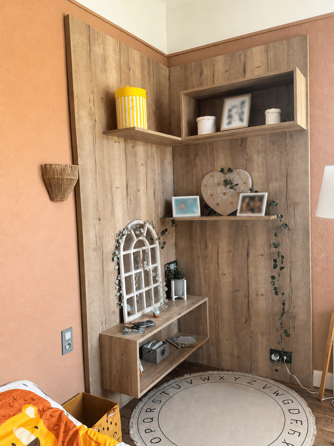 Étagère Murale d’Angle en Bois : Déco Chambre Enfant Étagère d'angle murale en bois avec décoration, miroir blanc et tapis alphabet rond dans une chambre d'enfant.